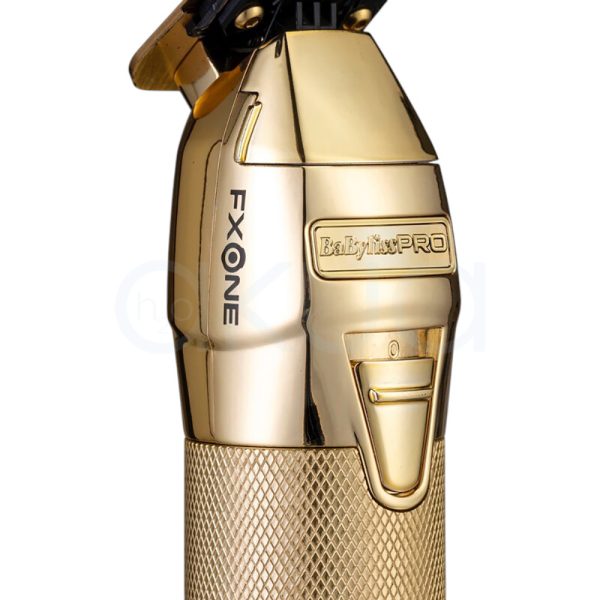 Maquina FXONE Gold Trimmer Babyliss Pro El color predominante es dorado metálico, presente tanto en el cuerpo principal de la máquina de corte como en la base del cargador y el mango del dispositivo. El recortador y la base tienen una textura grabada en dorado, lo que aporta un acabado elegante y lujoso. El cartucho de batería muestra detalles en azul translúcido con inscripciones en negro, añadiendo un contraste moderno al conjunto. Hay pequeños detalles en negro en la parte superior de la cuchilla y en la base del cargador, así como inscripciones en negro y azul en la batería H2o Akua