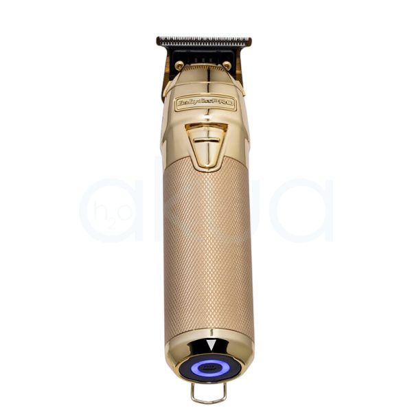 Maquina FXONE Gold Trimmer Babyliss Pro El color predominante es dorado metálico, presente tanto en el cuerpo principal de la máquina de corte como en la base del cargador y el mango del dispositivo. El recortador y la base tienen una textura grabada en dorado, lo que aporta un acabado elegante y lujoso. El cartucho de batería muestra detalles en azul translúcido con inscripciones en negro, añadiendo un contraste moderno al conjunto. Hay pequeños detalles en negro en la parte superior de la cuchilla y en la base del cargador, así como inscripciones en negro y azul en la batería H2o Akua