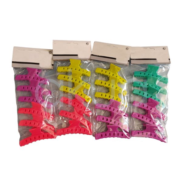 Pinza separadora 8,3cm ondina 6unid H2oAkua Se presenta en paquetes de pinzas plásticas para el cabello en colores brillantes y variados. Se observan pinzas de color rosa, rojo, amarillo y verde turquesa, organizadas en bolsas transparentes, cada una con una combinación de estos tonos vivos y llamativos.