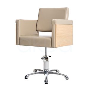 Sillon Rustik Beige H2oAkua. La imagen muestra una silla de peluquería profesional de diseño moderno y minimalista. Tiene estructura cuadrada, tapizada en polipiel color beige, con apoyabrazos rectos que combinan el mismo tapizado y paneles laterales en acabado madera clara. El respaldo es también tapizado y presenta una ligera inclinación para mayor comodidad. La base es metálica, cromada y en forma de estrella con cinco patas, dotada de un sistema hidráulico ajustable en altura.