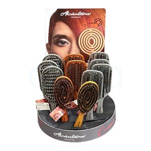 Expositor 12 cepillos Gold Brush Alcantara 100% cerdas Jabali. El expositor es un mostrador circular de sobremesa, de color negro en la base, donde se lee la marca “Alcántara Cosmética” en letras blancas. Sobre la base se disponen varias filas de cepillos o peines de pelo de mango ancho y cerdas oscuras, colocados en posición vertical y acompañados de pequeñas etiquetas colgantes; en la parte trasera se ve un cartel publicitario alto con una imagen promocional parcialmente difuminada. H2o Akua