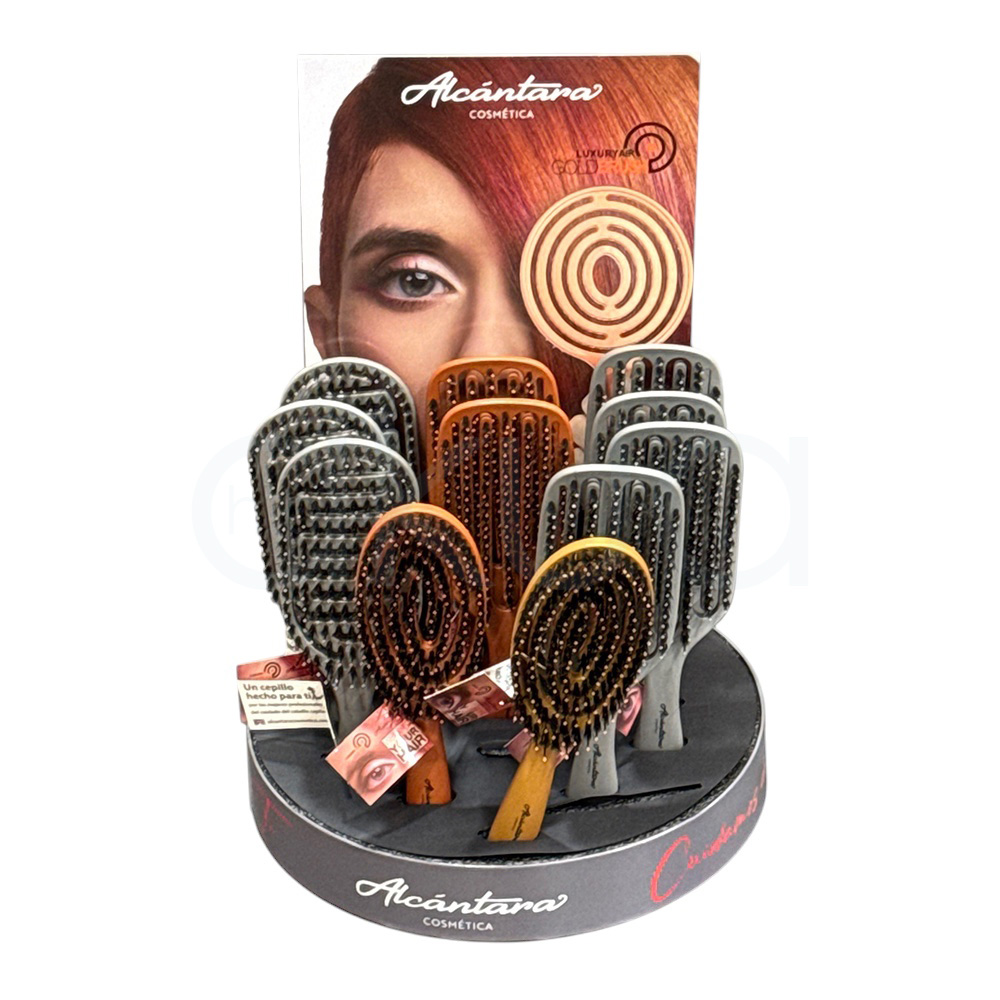 Expositor 12 cepillos Gold Brush Alcantara 100% cerdas Jabali. El expositor es un mostrador circular de sobremesa, de color negro en la base, donde se lee la marca “Alcántara Cosmética” en letras blancas. Sobre la base se disponen varias filas de cepillos o peines de pelo de mango ancho y cerdas oscuras, colocados en posición vertical y acompañados de pequeñas etiquetas colgantes; en la parte trasera se ve un cartel publicitario alto con una imagen promocional parcialmente difuminada. H2o Akua