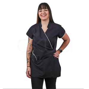 Kimono antibacteriano negro ribete plata jp. Casaca tipo kimono de trabajo en color negro liso, de manga corta y corte recto hasta la cadera. Lleva un escote cruzado en V ribeteado con vivo plata fino que también aparece en el borde de las mangas, y en la parte baja tiene grandes bolsillos frontales. H2o Akua