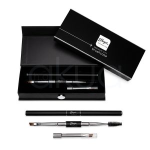 Pinceles Premium Dye Thuya. La imagen muestra un estuche premium "Brushcase Dye" de Thuya, caja negra rígida satinada semiabierta con logo blanco Thuya y texto "Premium Dye Brushcase". Dentro, 4 pinceles profesionales de mangos metálicos negros brillantes con detalles plateados: dos angulares para cejas (cerdas firmes), uno de precisión fina y un cepillo spoolie (fibra densa). Están dispuestos elegantemente sobre fondo negro aterciopelado interior. H2o Akua