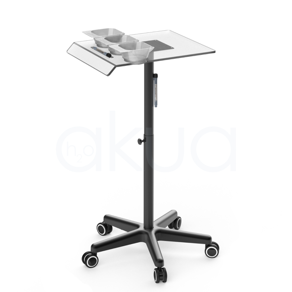 Carrito auxiliar Velura H2oAkua. Carrito auxiliar profesional de peluquería con estructura metálica negra y bandeja superior transparente. La bandeja incorpora tres recipientes para mezcla de tintes o tratamientos capilares, un soporte lateral para documentos o tabletas y un espacio destinado a herramientas de trabajo. Cuenta con columna central regulable en altura mediante pomo de ajuste y una base de cinco brazos con ruedas giratorias que facilitan su movilidad. Su diseño moderno y funcional está pensado para optimizar la organización de productos y accesorios durante servicios de coloración, tratamientos capilares y trabajos técnicos en peluquería.