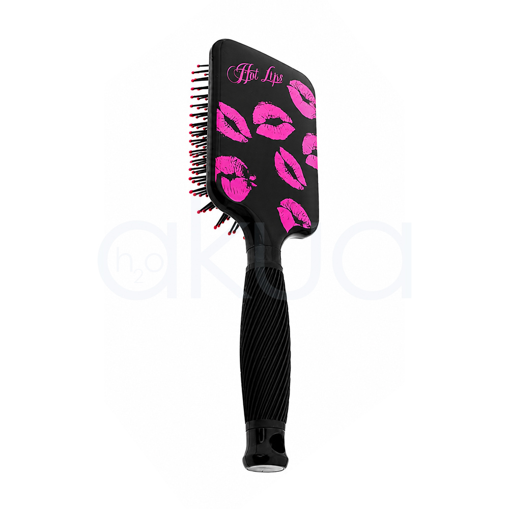 Cepillo desentedante Kisses Giubra. Cepillo paddle desenredante de color negro con diseño decorativo de labios en tonos rosa fucsia impresos sobre la parte trasera del cabezal. En la esquina superior izquierda aparece la frase "Hot Lips" escrita en letra cursiva rosa. El cepillo cuenta con púas negras flexibles terminadas en pequeñas bolitas rosas para un cepillado suave del cuero cabelludo. Su mango ergonómico negro presenta un acabado estriado que mejora el agarre y un orificio en el extremo para colgarlo. La imagen está tomada sobre un fondo claro, destacando el contraste entre el negro brillante del cepillo y los detalles decorativos en color rosa. H2o akua